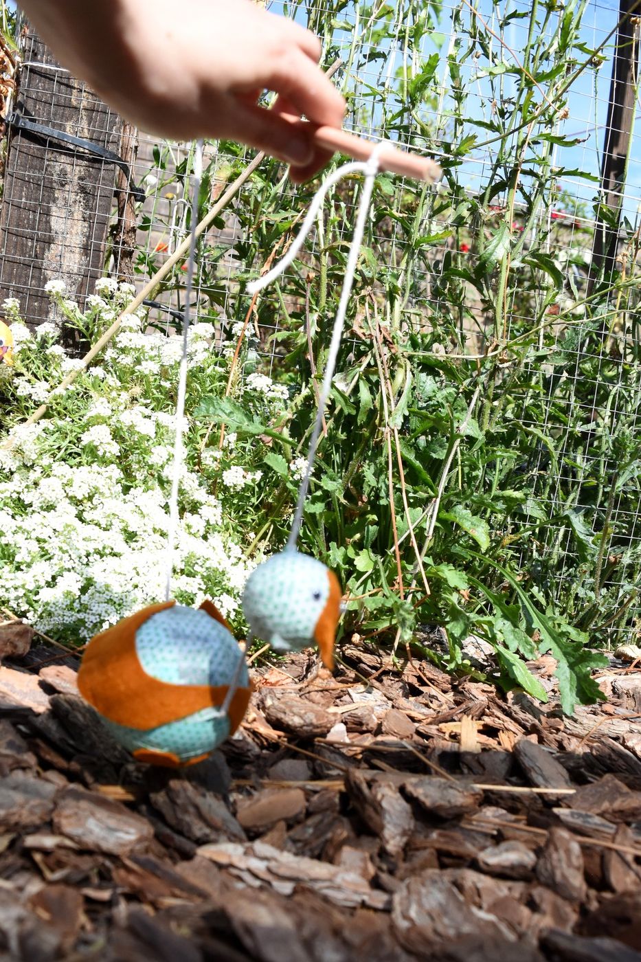 Two small bird puppets on strings held over garden plants
