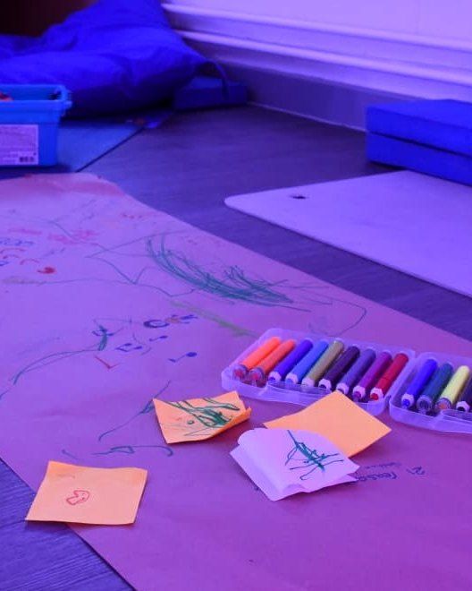 Workshop floor with a long paper drawing and crayons in purple light