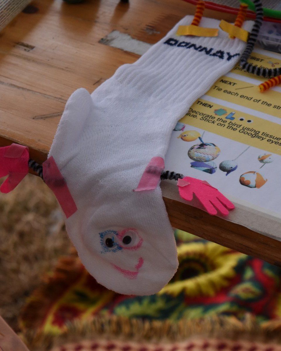 White sock puppet with pink paper hands hanging off a wooden table