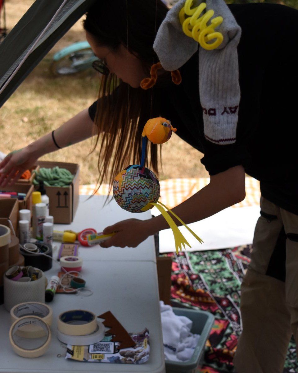 Facilitator at a workshop table with tape, scissors, yarn and hanging bird puppets