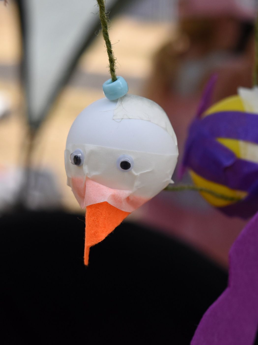 White ping-pong bird puppet hanging on string, orange felt beak