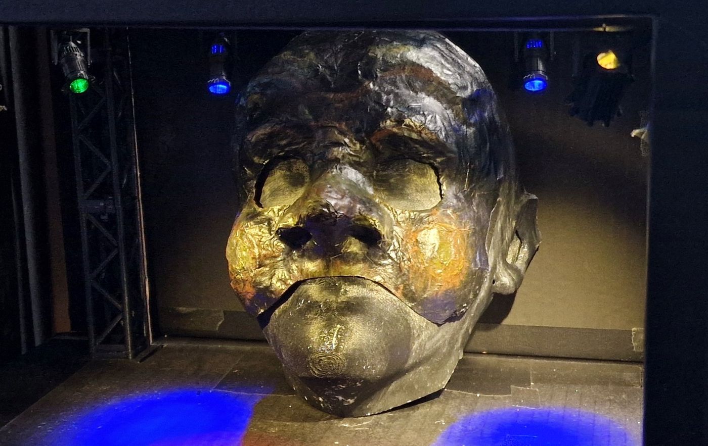Sculpted mask under gold and blue stage light in a model box