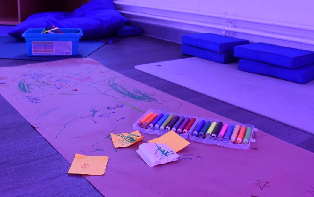 Workshop floor with a long paper drawing, crayons and floor cushions in purple light