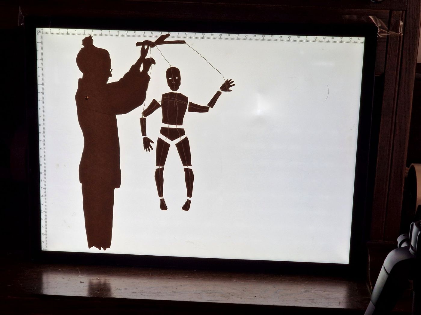 Cut-paper silhouette of a puppeteer working a jointed marionette on a light table
