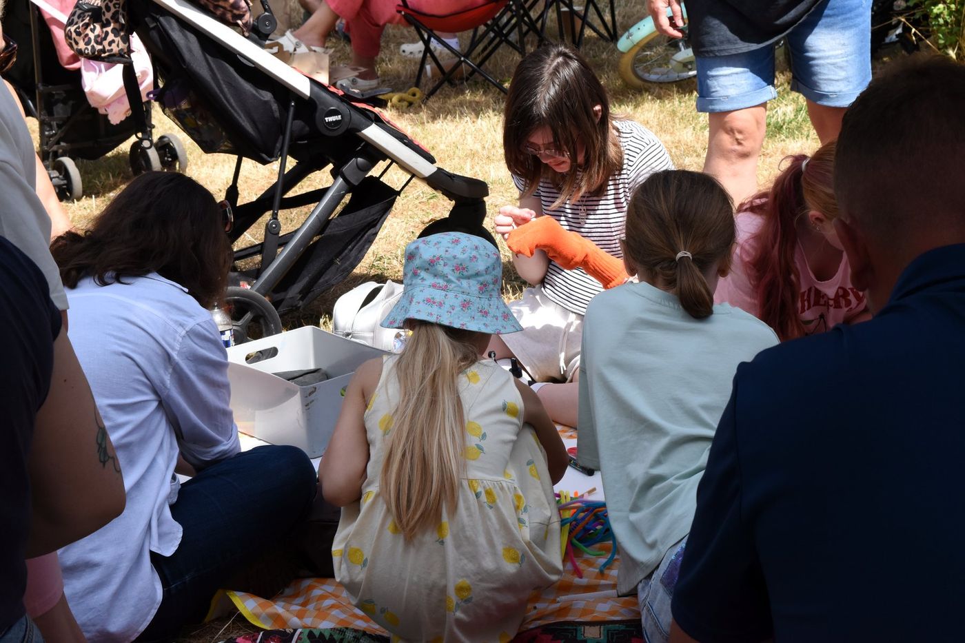 Outdoor puppet-making circle on a picnic blanket, materials in the middle